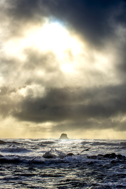 Lone sea stack at Ruby Beach silhouetted against a dramatic stormy sky with god rays breaking through